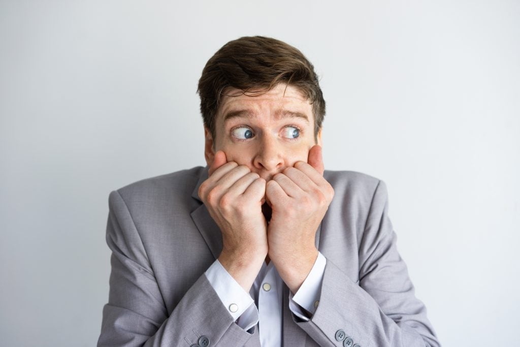 Desperate and scared businessman keeping silence. Concerned young Caucasian man covering mouth with hands and looking away. Fear or panic concept