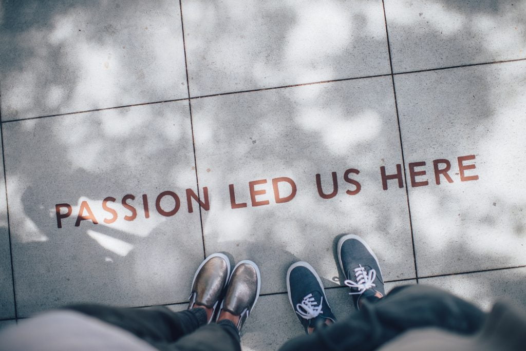 Two people looking down at the phrase "Passion Led Us Here" written on the sidewalk, representing a passion for learning, expanding our Learning Quotient