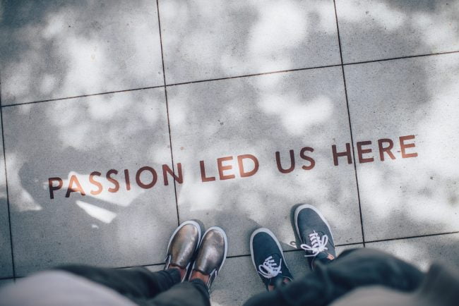 Two people looking down at the phrase "Passion Led Us Here" written on the sidewalk, representing a passion for learning, expanding our Learning Quotient