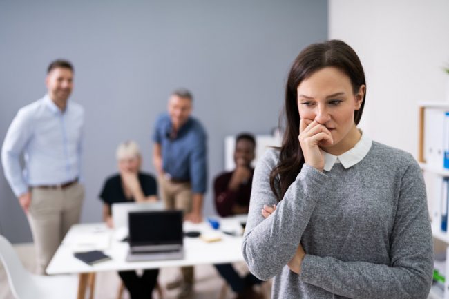 Gaslighting in the workplace, depicted by young woman being laughed at by work colleagues